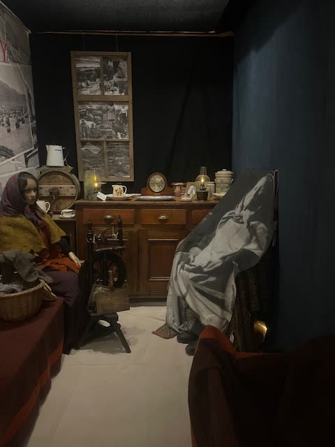 Inside the blackhouse exhibit, with a spinning wheel, dresser and figure by the fireside
